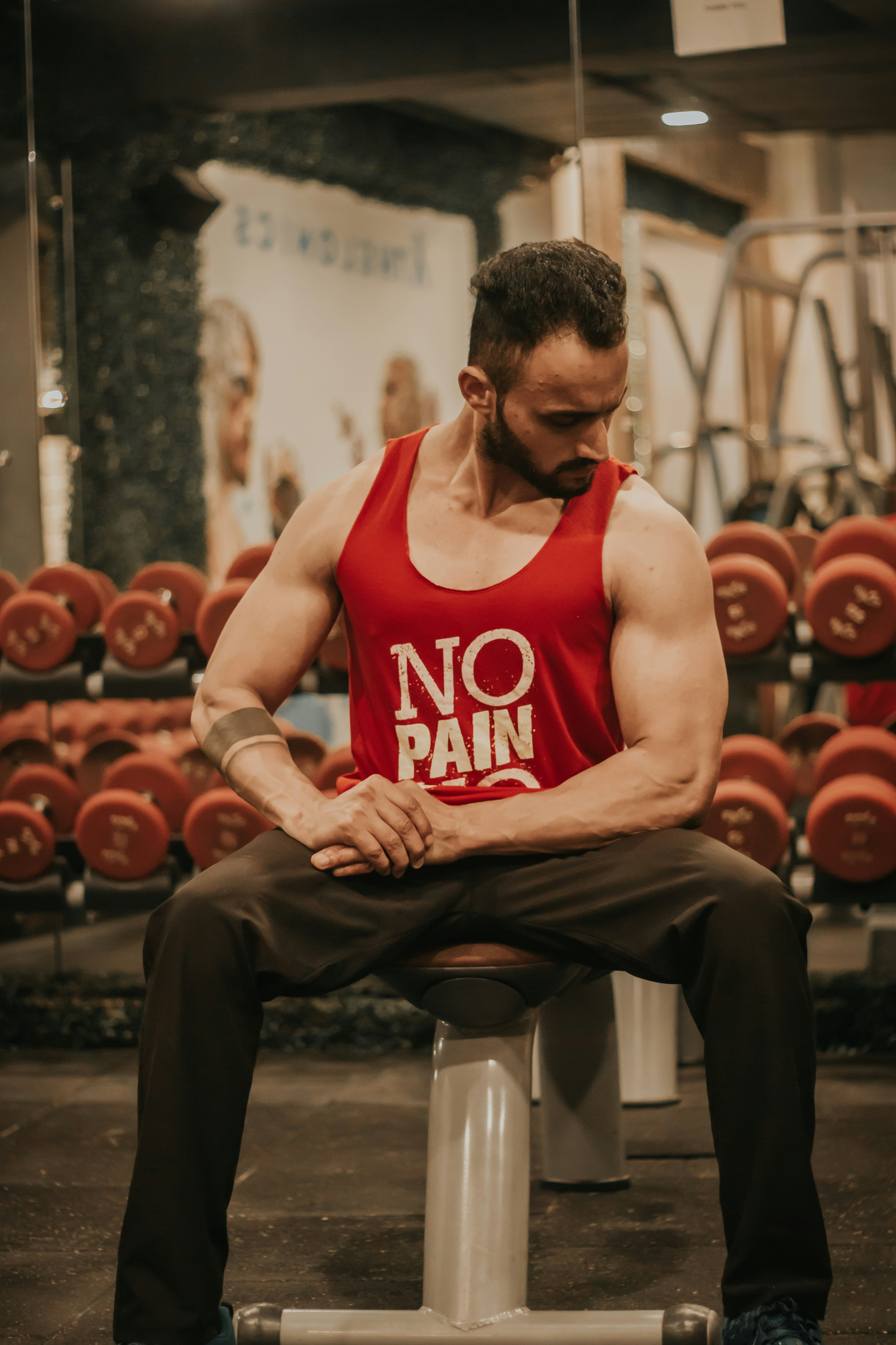man in red tank top and black pants sitting on bench